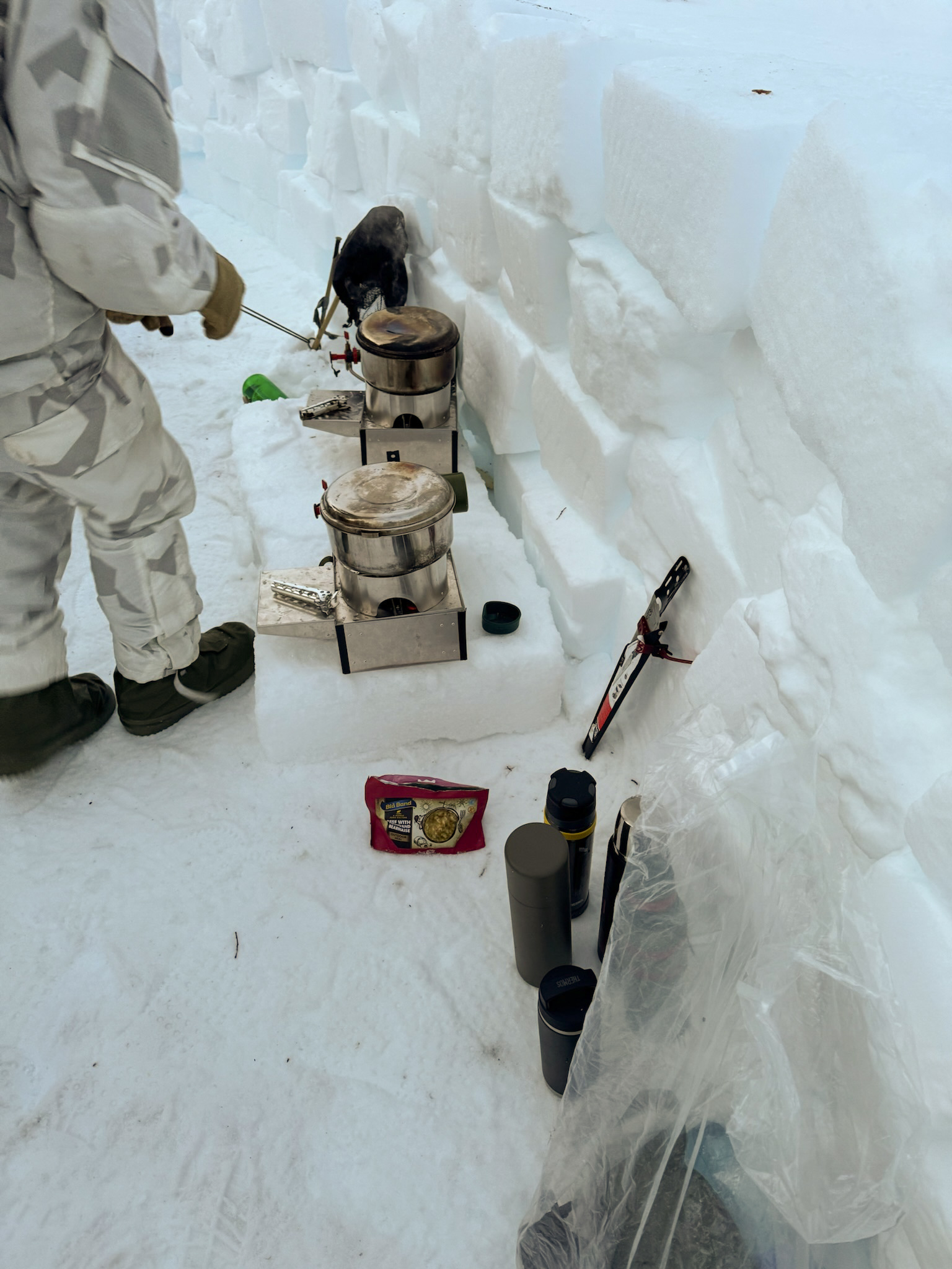 Two Fyringsvakta stoves with pots on a ledge in a field kitchen cut from snow blocks.